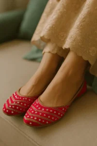 Traditional red khussa shoes with gold embroidery and white embellishments, styled with beige ethnic wear—perfect for bridal fashion, festive outfits, and luxury handcrafted footwear.
