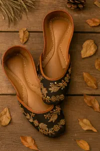Black embroidered khussa shoes for women with golden floral detailing, handcrafted ethnic footwear on rustic wooden background with autumn leaves.
