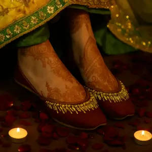 Bridal red khussa shoes with gold embroidery worn with henna-adorned feet, surrounded by rose petals and candles for traditional wedding ceremony
