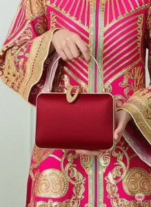 Woman in pink and gold embroidered outfit with floral and geometric patterns, holding elegant red handbag with gold clasp – luxury ethnic fashion and accessories