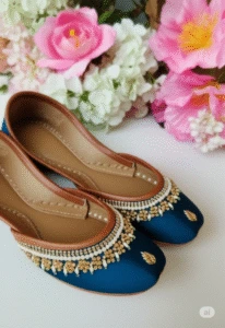 Blue and gold embroidered khussa juttis for women – traditional Indian footwear with beadwork, displayed on white surface with floral decor, perfect for weddings and festive wear