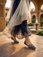 Bridal khussa for women walking through a Mughal-style courtyard, navy blue embroidered bridal shoes in motion