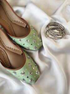 Mint green embroidered khussa jutti placed with silver bangles on white fabric — bridal footwear Pakistan