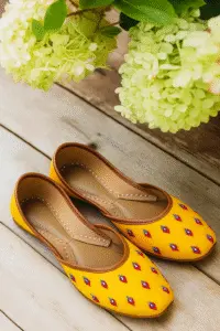 Mustard yellow hand embroidered khussa jutti with diamond motif placed near white flowers, Pakistan