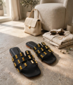 Black flat slippers with gold stud detailing styled with handbag, sunglasses and linen outfit