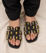 Black studded flat sandals for women with gold pyramid studs worn with black trousers