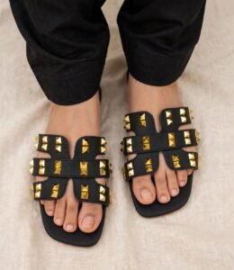 Black studded flat sandals for women with gold pyramid studs worn with black trousers