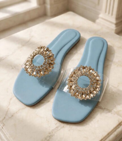 Close-up of gold crystal detail on blue ladies flat slippers with clear PVC strap