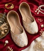 Top view of golden bridal khussa shoes on red velvet with pearl and gold jewelry