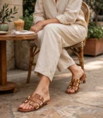 Woman wearing tan brown ladies studded flat sandals with gold studs and a beige linen outfit at a cafe