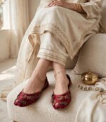 Woman wearing maroon embroidered khussa with a cream embroidered shalwar kameez and gold bangles