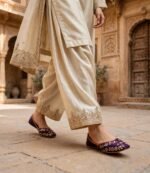 Woman walking in purple embroidered khussa shoes with cream embroidered shalwar kameez