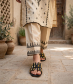 Woman walking in black studded flat sandals with cream embroidered Pakistani kurta and trouser