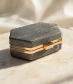 Charcoal grey glitter box clutch with golden metal frame and clasp on cream marble