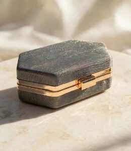 Charcoal grey glitter box clutch with golden metal frame and clasp on cream marble