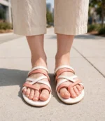 Front view of women's coral and white strappy flat sandals worn with beige linen pants