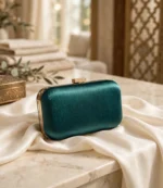 Green satin box clutch with gold clasp styled on marble table with ivory fabric