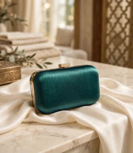Green satin box clutch with gold clasp styled on marble table with ivory fabric