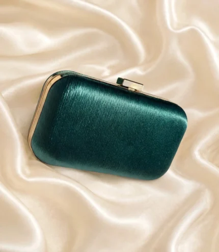 Emerald green clutch bag with textured satin finish and gold frame on cream silk