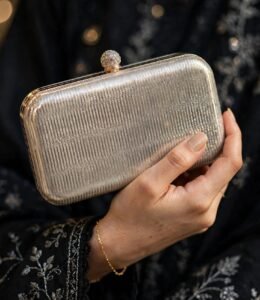 Hand holding formal box clutch bag with black embroidered outfit