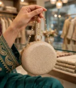 Hand holding golden glitter round clutch bag by its rhinestone chain