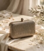 Ribbed metallic ladies clutch bag with gold frame beside jewellery