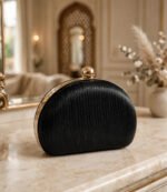 Black pleated half moon ladies evening clutch bag with gold ball clasp on marble