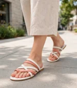 Woman walking in coral pink and white strappy toe-ring flat sandals with linen trousers