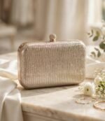 Golden shimmer party wear clutch bag with crystal clasp on marble table