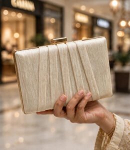 Hand holding ivory party wear clutch bag with gold clasp and bangles