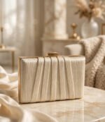 Ivory pleated party wear clutch bag with gold frame on marble table