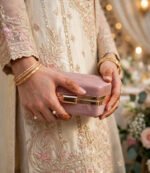 Woman in embroidered wedding outfit holding rose pink glitter box clutch with gold kiss-lock