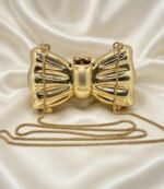 Gold bow clutch bag with long gold chain strap on cream satin