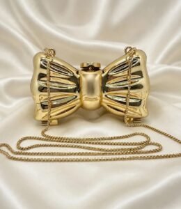 Gold bow clutch bag with long gold chain strap on cream satin