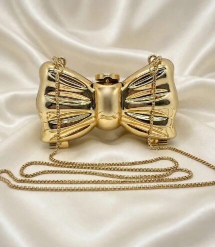 Gold bow clutch bag with long gold chain strap on cream satin