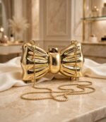 Gold bow clutch bag for women displayed on marble with ivory silk