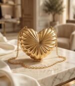 Gold heart clutch bag with chain strap displayed on cream marble table