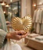 Golden heart shaped clutch with gold chain held by woman in embroidered sage green suit