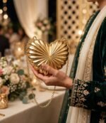 Woman with mehndi holding golden heart shaped clutch at wedding in green velvet suit