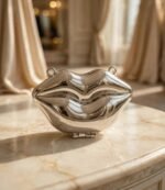 Mirror-finish metallic lip clutch bag with hinge detail on a marble table