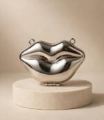 Silver lip clutch bag with side rings for a chain strap on a stone stand
