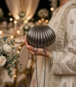 Woman in embroidered cream outfit holding shell wedding clutch bag